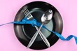 © Jumain - Healthy eating or dieting concept. fork and spoon wrapped in blue measuring tape on empty plate with crossed position. isolated background.