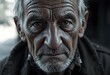 © Yurii - Close-up portrait of an elderly man with deep wrinkles on his face, gray hair, and a serious, contemplative expression, wearing a dark jacket.