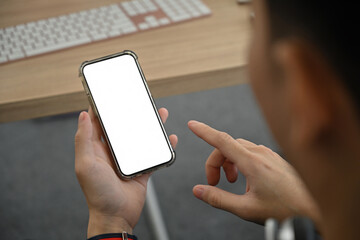 Poster - Close-up of a person holding a smartphone with a blank white screen, ideal for mockups or app presentations in a creative office environment