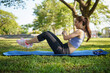 © matinee - Active young woman doing ab workout on yoga mat in a green park during morning exercise.