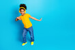 © deagreez - Cheerful young girl dancing with yellow headphones on a blue background, showcasing youthful energy and vibrant style