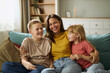 © Goran - Happy single mother having fun with her joyful children on sofa at home. She is looking at camera