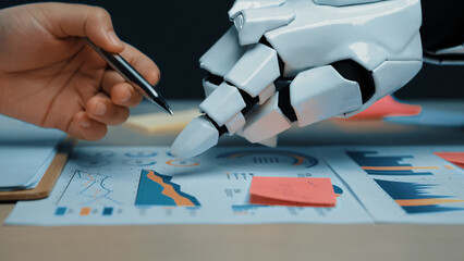 Poster - A human hand and a robotic hand work together on business charts, analyzing data trends and showcasing the fusion of technology and human creativity in the workplace.Noogenesis
