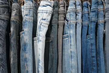 Aufkleber - Row of jeans are hanging on a rack. The jeans are of different colors.
