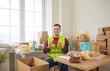 © Studio Romantic - Smiling young volunteer holding red heart in hands sitting at charity center packing donations of foodstuffs in cardboard boxes. Man volunteering in charitable foundation. Humanitarian aid concept