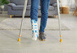 © Studio Romantic - Cropped image of unrecognizable man has broken leg, walking on crutches, wearing fracture fixator, walking in living room at home. Focus on human feet. Physical injuries and rehabilitation