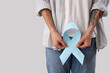 © Pixel-Shot - Young man with blue ribbon on light background, closeup. Prostate cancer awareness concept