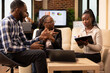 © DC Studio - African American startup team gathers around, reviewing documents in modern workspace. Professional black woman explains marketing strategies on clipboard during business meeting.