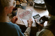 © AnnaStills - Senior Caucasian woman and senior Black man reviewing overdue utility bill with past due notice, holding paperwork and using calculator at kitchen table, focusing on financial stress