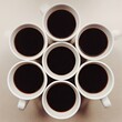 © asAI12 - Seven white mugs filled with dark coffee arranged in a circular pattern on a light beige surface, viewed from directly above