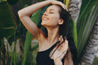 © SHOTPRIME STUDIO - Tropical elegance Woman in black dress standing by palm tree with windblown hair