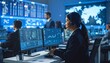 © photostockatinat - An office environment with focused individuals working on computers, possibly a control room or a technical setting. The scene depicts data analysis, system monitoring, or information processing.
