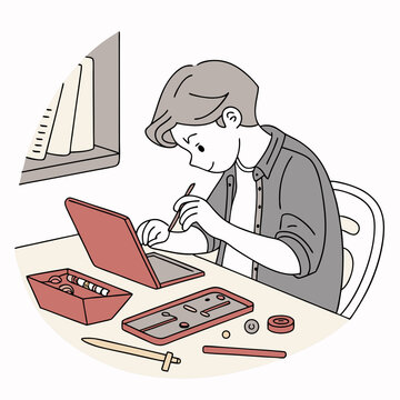 A young boy is sitting at a desk using a stylus on a laptop with craft supplies and books nearby him