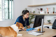 © itchaznong - Veterinary Care and Technology. A veterinarian examining a patient's records on a computer while a dog observes.