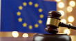 © MuhammadArslan - A wooden gavel rests against a blurred European Union flag backdrop, suggesting law, legislation, and judicial proceedings within the EU.