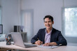 © Apichat - A man in a suit is sitting at a desk with a laptop and a pen