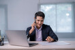© Apichat - A man in a suit is talking on his cell phone while sitting at a desk
