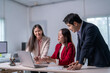 © Apichat - Three people are sitting at a desk with a laptop open