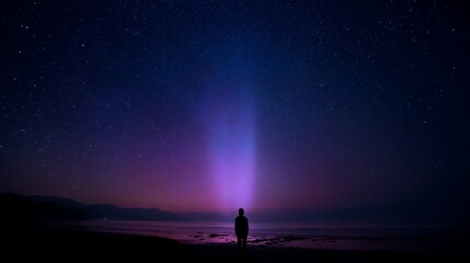 Poster - Person stands on dark beach under a starry sky with colorful light beam emanating from the horizon at night