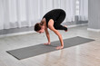 © TRAVELARIUM - Young caucasian woman performing crow pose on mat in serene, light-filled yoga studio. Neutral environment enhances focus and balance, evoking calm and concentration