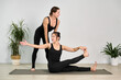 © TRAVELARIUM - Two women, young asian woman stretching on mat and young white instructor guiding her, practice yoga in serene studio. Calm ambiance, minimalistic decor