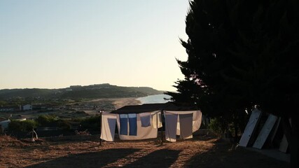 Poster - Laundry hangs on a line in a sunny area near the coast, with the beach and hills visible as the sun sets, highlighting a tranquil summer evening