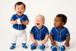 © OlenaSpark - Three diverse toddlers in matching blue-and-white baseball uniforms sitting and smiling. One toddler holds a baseball. Concept of childhood sports, fun, and early education.