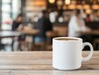 © Noppakun - A white ceramic coffee mug filled with coffee sits on a wooden table in a cozy cafe with blurred people and warm lights in the background.