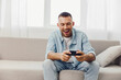 © SHOTPRIME STUDIO - Happy man enjoying a digital detox while playing games on his phone, showcasing a moment of relaxation and engagement with technology at home.