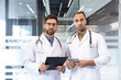 © Liubomir - Two male doctors stand together, one holding a clipboard and the other a tablet, in a modern medical environment.