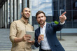 © Liubomir - Two businessmen in front of a modern building discussing a project, one pointing the other holding a tablet.
