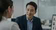 © Luiz - A man in a suit smiles at a woman in an office setting with a computer screen visible nearby