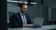 © Luiz - Man with glasses and suit working on a laptop in an office cubicle with a serious expression