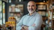 © An - A bald man with a beard standing in a coffee shop with arms crossed.
