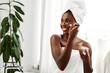 © fotofabrika - Woman applying skincare routine while smiling in a bright, fresh bathroom with white decor