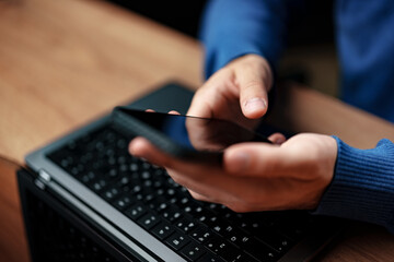 Poster - Person using smartphone while sitting at desk with laptop in modern workspace