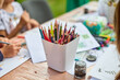 © TRAVELARIUM - Child painting colorful drawings on wooden surface. Bright pencils in focus. Casual indoor setting with natural light enhancing creativity