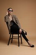 © New Africa - Beautiful woman in stylish outfit sitting on chair against beige background
