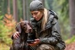 © Gatherina - Hunter woman using smartphone with her dog in forest during rain