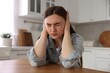 © New Africa - Scared woman suffering from paranoia at wooden table in kitchen