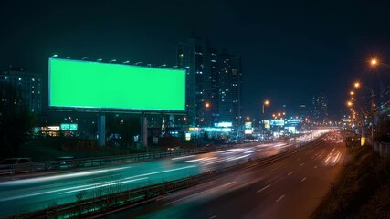 Poster - Green chroma key billboard advertising panel by night with car light trails and illuminated cityscape in the background, perfect for showcasing your message to passing drivers
