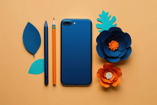 Flat lay of a blue smartphone with paper flowers and pencils on a peach colored background