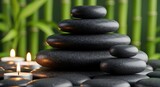 Stacked black spa stones with lit candles and green bamboo background for relaxation and wellness concept
