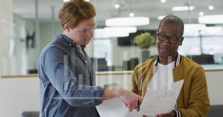 Poster - Standing two male professionals reviewing printed charts with digital graph overlay in office space