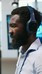 Poster - Vertical video Computer scientist in office integrating AI machine learning systems to streamline workflows, earing headphones. African american man uses artificial intelligence on devices, listening