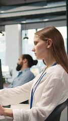 Fototapete - Vertical video Junior dev developing software applications, optimizing code for performance, listening music. Young female engineer wearing headphones in office using AI to resolve bottlenecks, camera