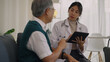 © Lifehdfilm - A young female doctor in a lab coat and stethoscope uses a tablet to discuss medical records with an elderly male patient in a bright clinic.