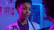 © Vizu - Professional woman with curly hair in white medical coat and purple top, wearing stethoscope, engaged in conversation in clinical setting with anatomical images, blue and purple lighting.