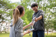 © bongkarn - Asian man in sportswear holding a water bottle getting it or giving to a woman at park's courtyard.