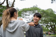 © bongkarn - Asian man and woman in sportswear smiling as elbow bumping together after running or jogging in park